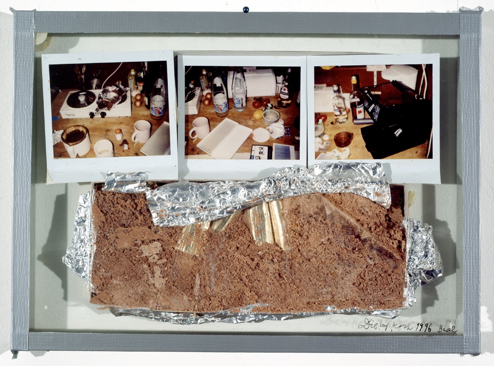 Dieter Roth, Hachez's Kleine, dreibebilderte Küchenszene (Hachez's small-three-illustrated Kitchen-scene), 1996/1998, chocolate in open packing, 3 polaroids (between two sheets of glass, grey adhesive tape), 26 × 35.7 × 2.5 cm